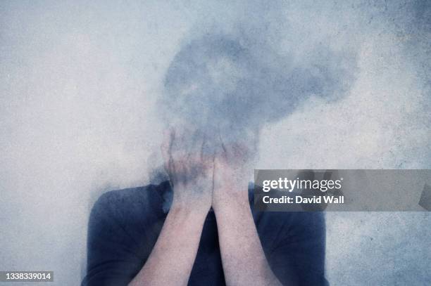 a mental health concept. of a man with his head in his hands vanishing into clouds. with a texture edit - desmoronar fotografías e imágenes de stock