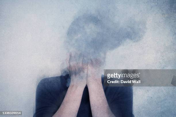 a mental health concept. of a man with his head in his hands vanishing into clouds. with a texture edit - deterioration stock pictures, royalty-free photos & images