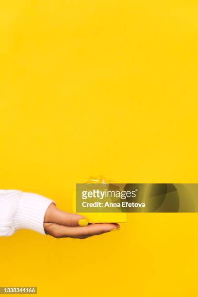 woman's hand is holding yellow gift box on yellow background. trendy colors of the year. front view - birthday present photos et images de collection