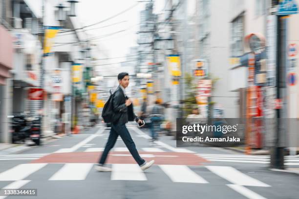 young japanese man in casual clothing crossing tokyo street - beenden stockfoto's en -beelden