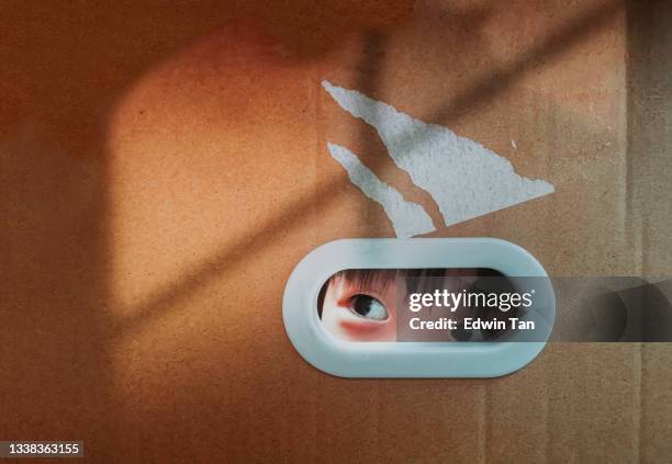 cute asian chinese baby boy peeking through ellipse hole on cardboard box hiding in cardboard box, looking out with window frame shadow - looking through hole stock pictures, royalty-free photos & images