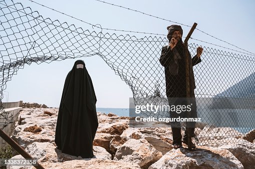 Refugee man and woman in burka standing behind a fence
