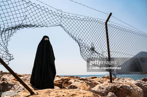 flüchtlingsfrau in burka hinter einem zaun stehend - flüchtlingslager stock-fotos und bilder