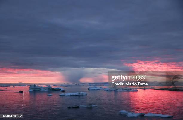 The sun sets as rain falls beyond floating ice and icebergs in Disko Bay above the Arctic Circle on September 04, 2021 in Ilulissat, Greenland. 2021...