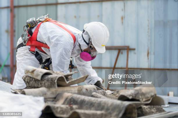 safety is our top priority. worker wearing full body protective clothing while working with the asbestos roof tiles. - asbestos stock pictures, royalty-free photos & images