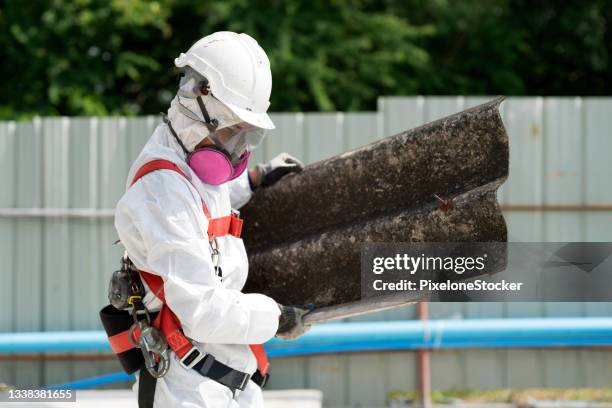 safety is our top priority. worker wearing full body protective clothing while working with the asbestos roof tiles. - asbestos removal photos et images de collection