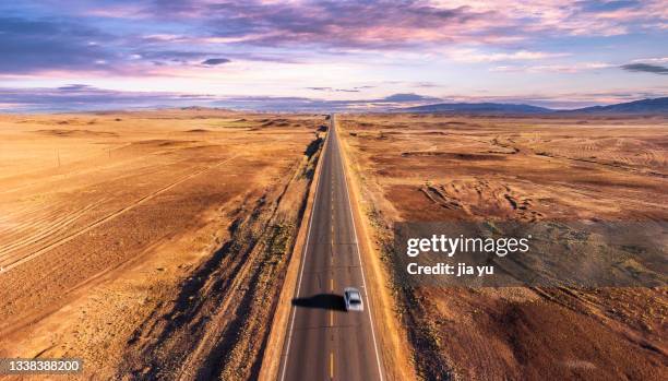 in the desolate desert area, a straight road leads to the distance, and a car is driving on the road. xinjiang, china. - wilderness road stock pictures, royalty-free photos & images