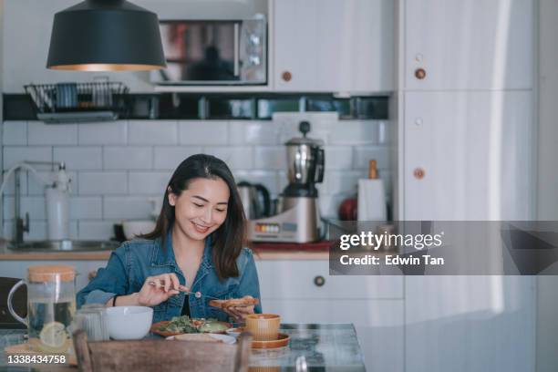 hermosa mujer china asiática disfrutando de su desayuno en casa untequillando pan integral mantequilla de maní con café - untar de mantequilla fotografías e imágenes de stock