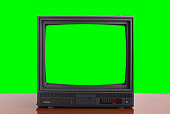 An old vintage 1970s TV with a green screen for adding video stands on a wooden table against a green background. Vintage TVs 1980s 1990s 2000s.