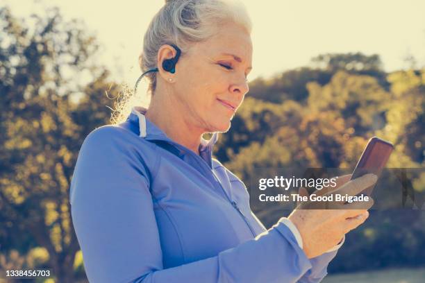 woman listening music on smart phone through headphones - mature women walking stock pictures, royalty-free photos & images