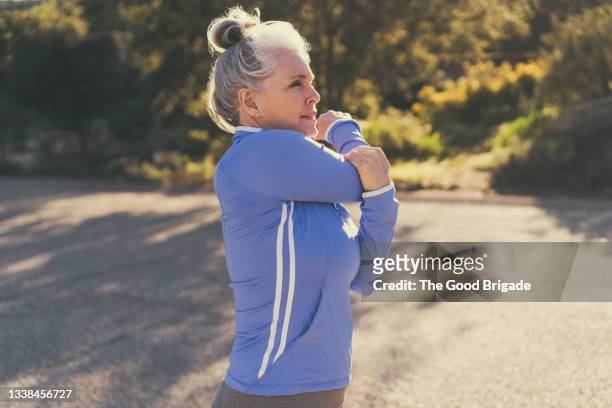mature woman stretching before exercise on sunny day - dehnen stock-fotos und bilder