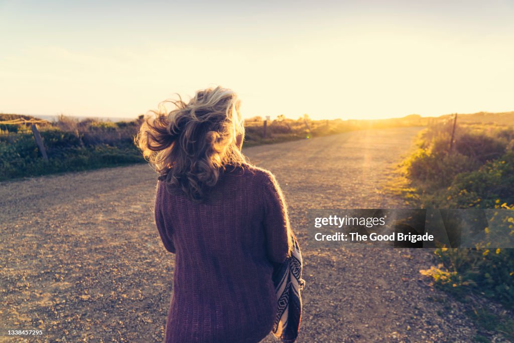 Rear view of woman walking on dirt road during sunset