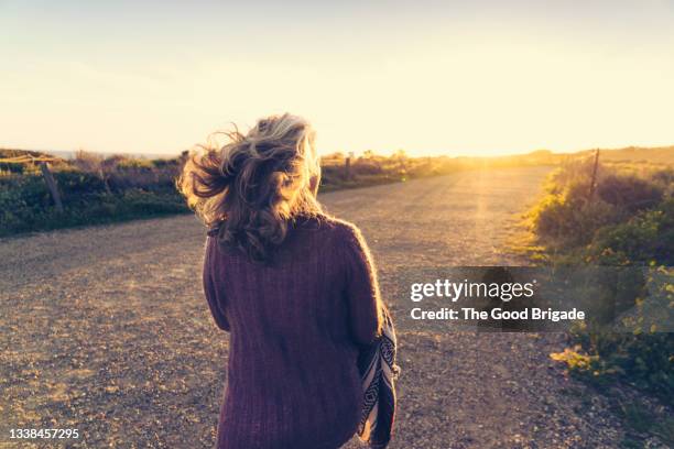 rear view of woman walking on dirt road during sunset - grey hair back stock pictures, royalty-free photos & images