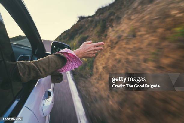 cropped image of woman waving hand through car window during road trip - car sunset arm stock pictures, royalty-free photos & images
