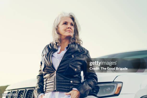 beautiful mature woman with hand in pocket against car - leather jacket stock pictures, royalty-free photos & images
