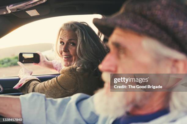 portrait of woman photographing while sitting in car during road trip - car interior sunset stockfoto's en -beelden