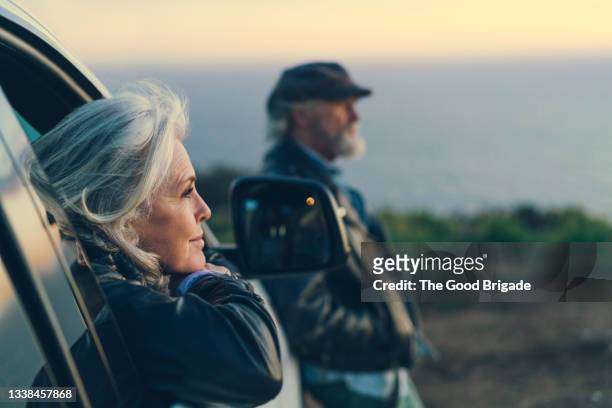 mature woman sitting in car during sunset - tranquility stock-fotos und bilder