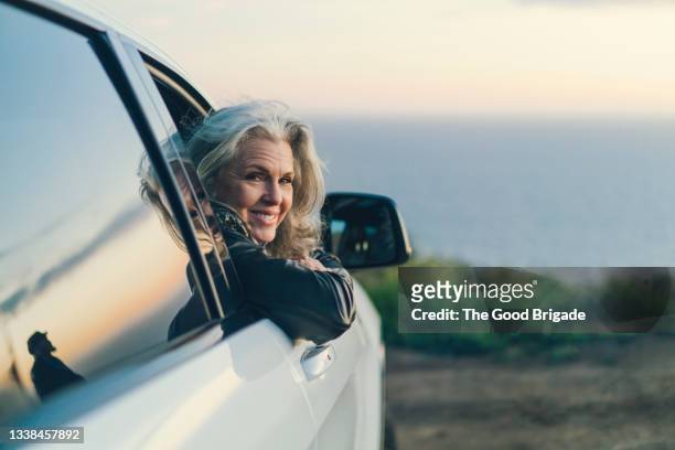 portrait of smiling woman leaning out car window - vrouw 50 jaar stockfoto's en -beelden