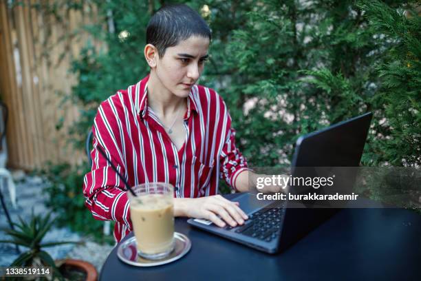 young bald business woman is relaxing with ice coffee and working on her laptop in cafe - turk telekom bildbanksfoton och bilder