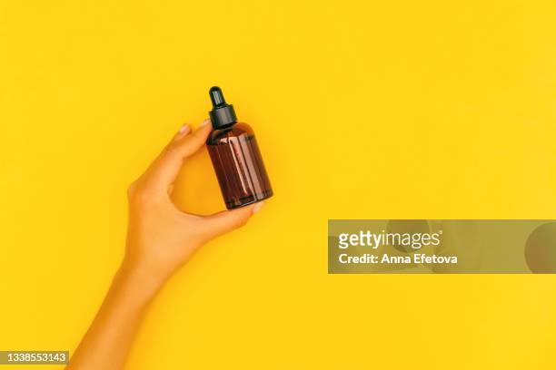 woman hand with manicure with gold pattern are holding amber glass bottle with cosmetic liquid on illuminating yellow background. trendy colors of the year 2021. body care concept. flat lay style. copy space for your design - argan oil stock-fotos und bilder