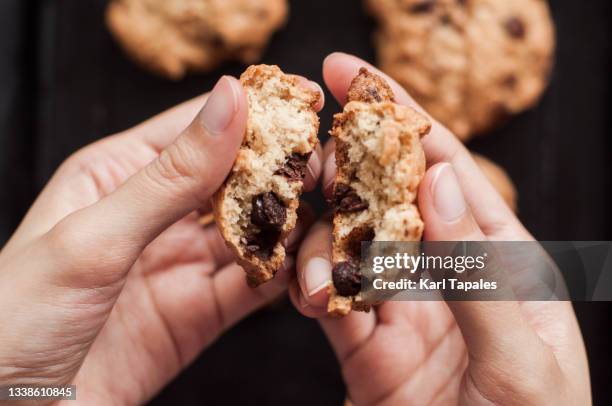 a young adult southeast asian woman is holding a freshly baked chocolate chip cookies from a baking pan - eating cookies foto e immagini stock