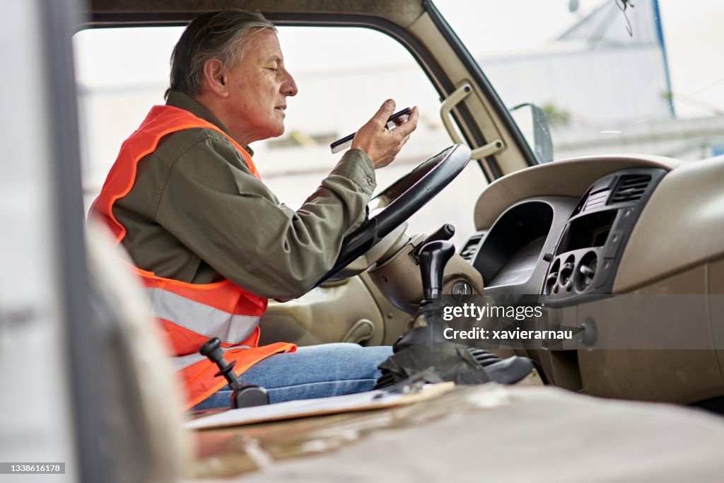 Mature Male Truck Driver Sitting in Vehicle and Using Phone