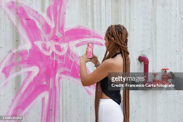 woman with braided hair taking a photo of the mural she is painting - graffiti mural stock pictures, royalty-free photos & images