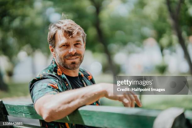 portrait of happy mature  man resting outdoors in park, looking at camera. - banco asiento fotografías e imágenes de stock