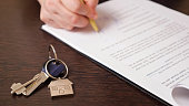 Man signs apartment purchase contract near keys at table