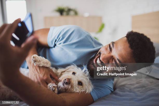 portrait of young man with dog on bed indoors at home, taking selfie. - african ethnicity lifestyle stock pictures, royalty-free photos & images