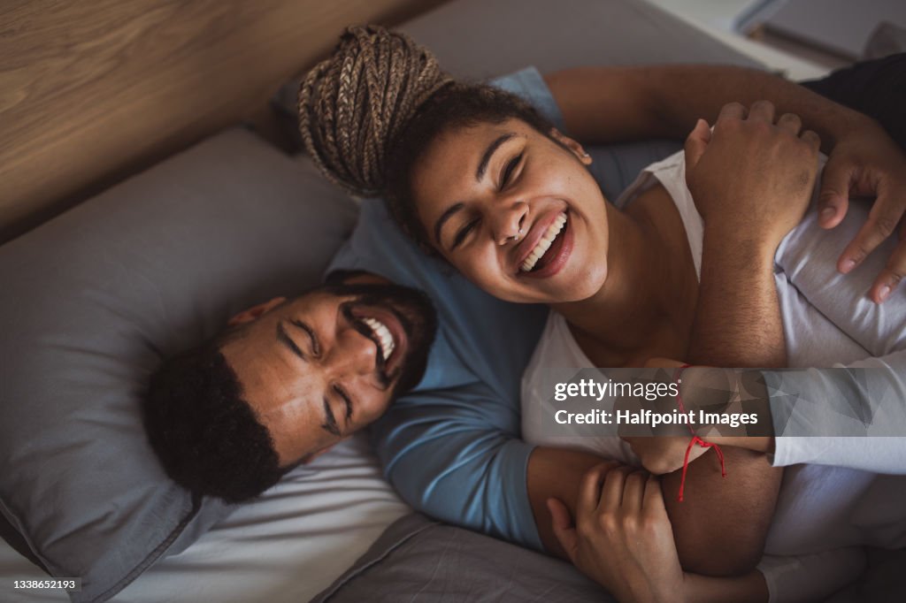 Portrait of young couple playing on bed indoors at home, laughing.