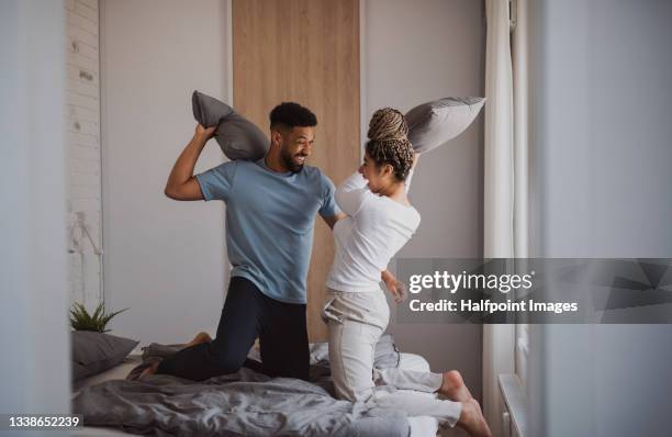 portrait of young couple playing on bed indoors at home, pillow fight. - luta de almofada imagens e fotografias de stock