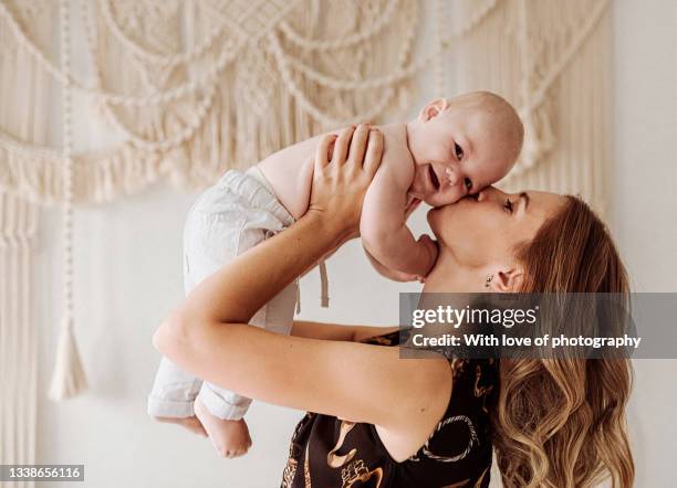 young adult beautiful mother with cute baby boy under 1 year macrmae arch boho style decor on background - buho stock pictures, royalty-free photos & images