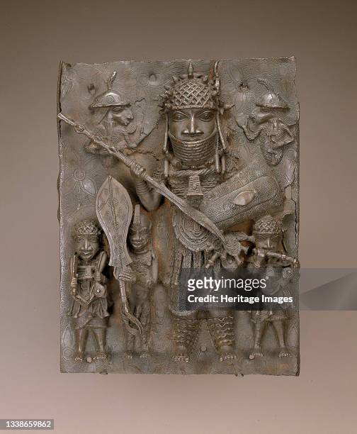 Copper alloy plaque with large central figure with shield, spear, beaded headdress and high collar flanked by nude male holding ceremonial sword,...