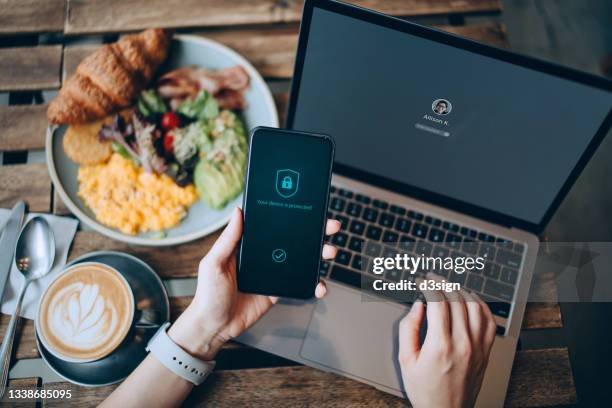 close up of businesswoman sitting in cafe having breakfast, logging in to her laptop and holding smartphone on hand with a security key lock icon on the screen. privacy protection, internet and mobile security concept - identity theft stock pictures, royalty-free photos & images