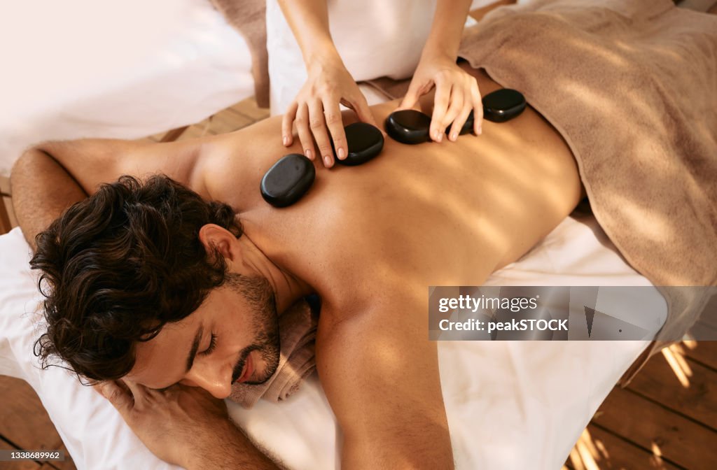 Handsome man at spa resort receives hot stone massage. Hot stone massage therapy using smooth, flat, heated stones