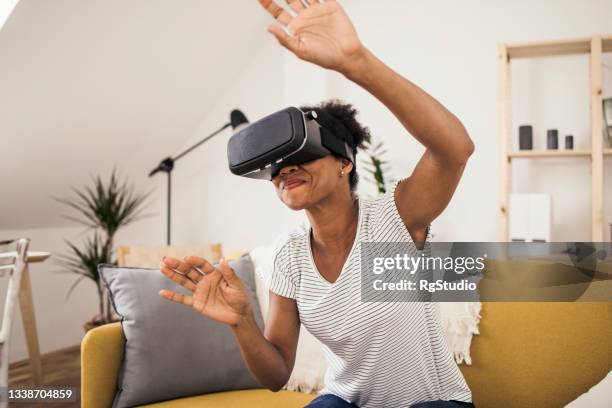 portrait d’une femme afro-américaine utilisant un casque de réalité virtuelle à la maison - flying goggles photos et images de collection