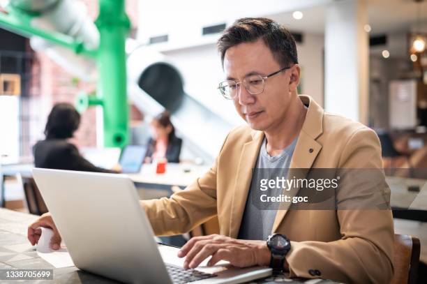 asiatischer chinesischer profi mittleren alters im business-anzug, der an seinem arbeitsplatz im co-working-büro arbeitet - chinese businessman stock-fotos und bilder