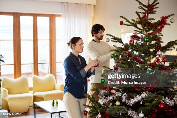 mid adult couple decorating christmas tree at home - decorating christmas tree stock pictures, royalty-free photos & images