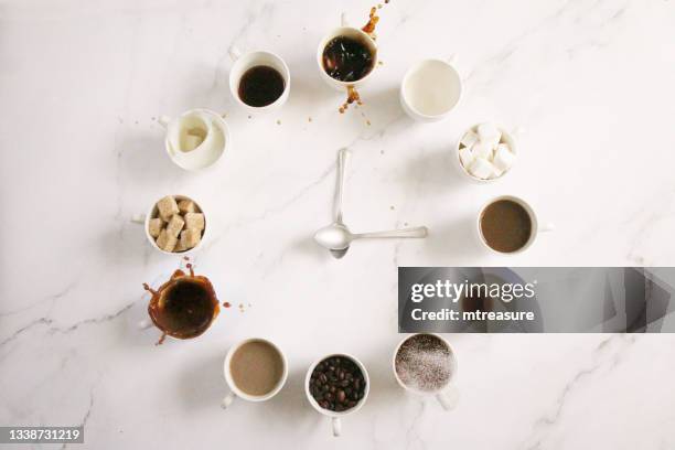 image of white, espresso cup clock face design , sugar cubes, milk, coffee and coffee beans in cups, teaspoon clock hands, overflowing, spraying, splashing droplets floating mid-air,  marble effect background, elevated view, copy space - coffee splash stockfoto's en -beelden
