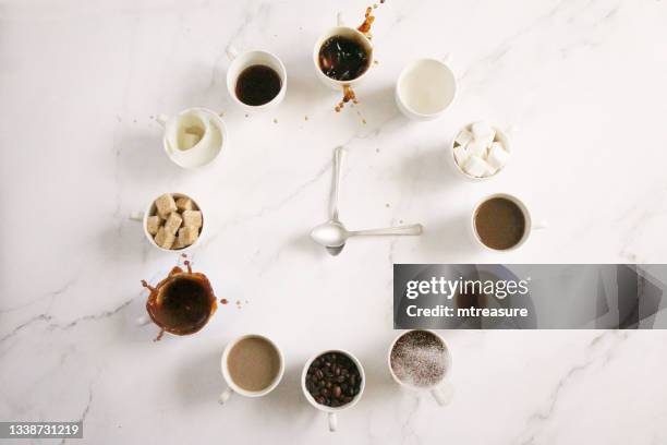 image of white, espresso cup clock face design , sugar cubes, milk, coffee and coffee beans in cups, teaspoon clock hands, overflowing, spraying, splashing droplets floating mid-air,  marble effect background, elevated view, copy space - milk tea cup stock pictures, royalty-free photos & images