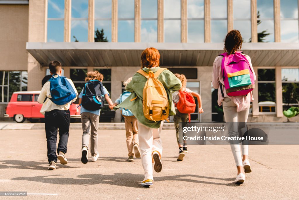 Little kids schoolchildren pupils students running hurrying to the school building for classes lessons from to the school bus. Welcome back to school. The new academic semester year start