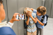 Schoolchildren cruel boys filming on the phone torturing bullying their classmate in school hall. Puberty difficult age