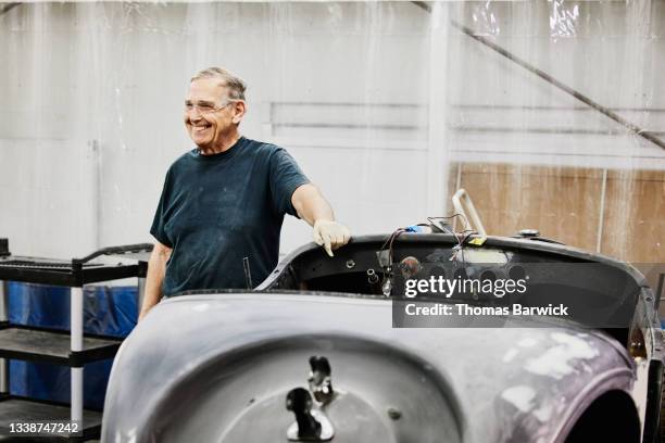 Medium wide shot of smiling man standing next to auto restoration project in community gaage body shop