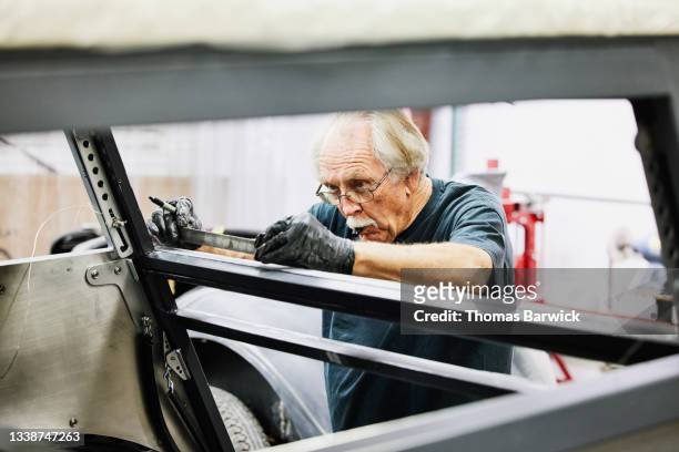 Medium shot of senior man measuring while working on auto restoration project in community garage