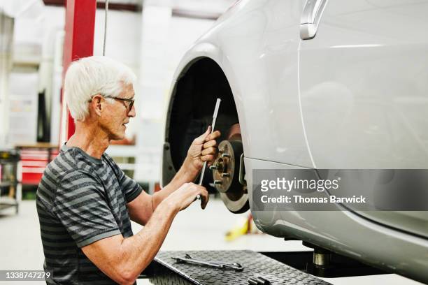 Medium shot of senior man working on car on lift in garage