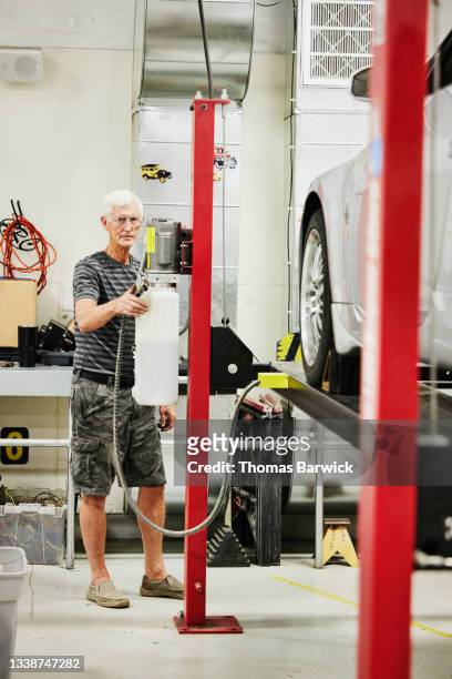 Wide shot portrait of senior man working on car on lift in garage