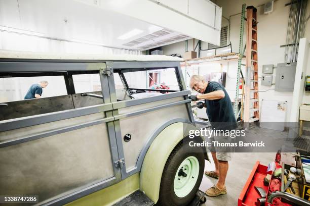 Wide shot of senior man preparing auto restoration for paint while working in community garage