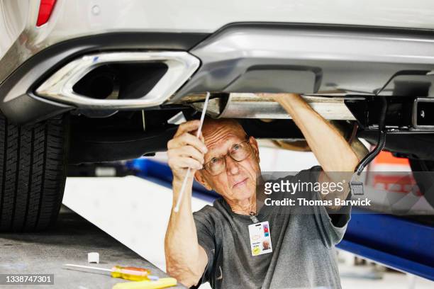 Medium shot of senior man working on car on auto lift in community garage