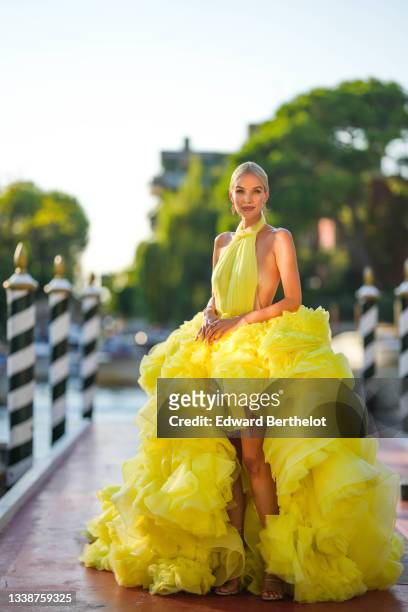 Leonie Hanne wears a yellow turtleneck lace off-shoulder back-nude gathered ruffled oversized party long dress, bejeweled earrings, during the 78th...